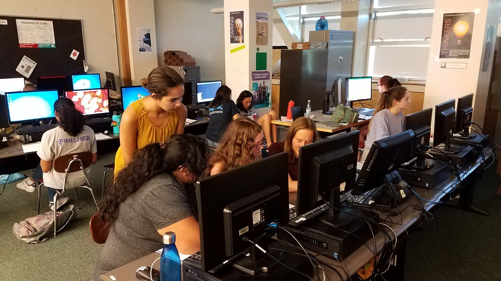 A group of students sitting in front of computers while being mentored by a educator
